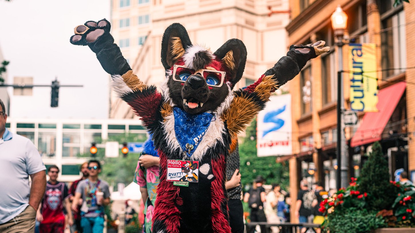 A fursuiter celebrating with their hands in the air at the Anthrocon 2023 Block Party.