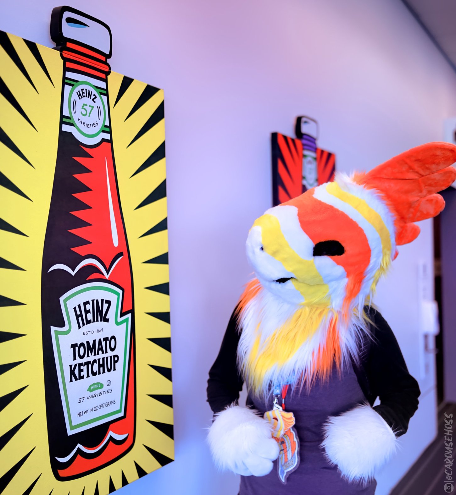 A fursuiter standing beside a contemporary piece of artwork featuring a Heinz ketchup bottle.