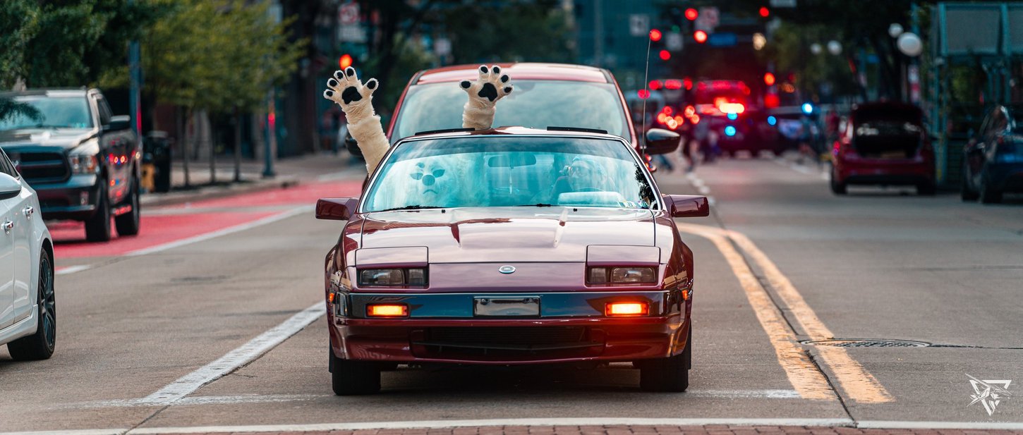 A fursuiter sticking their hands out of a car roof on Liberty Avenue in Pittsburgh.